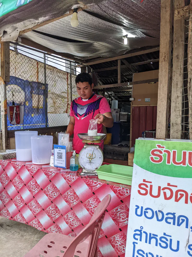 Vendor at a market stall using a scale to weigh goods and pack them into a plastic bag.