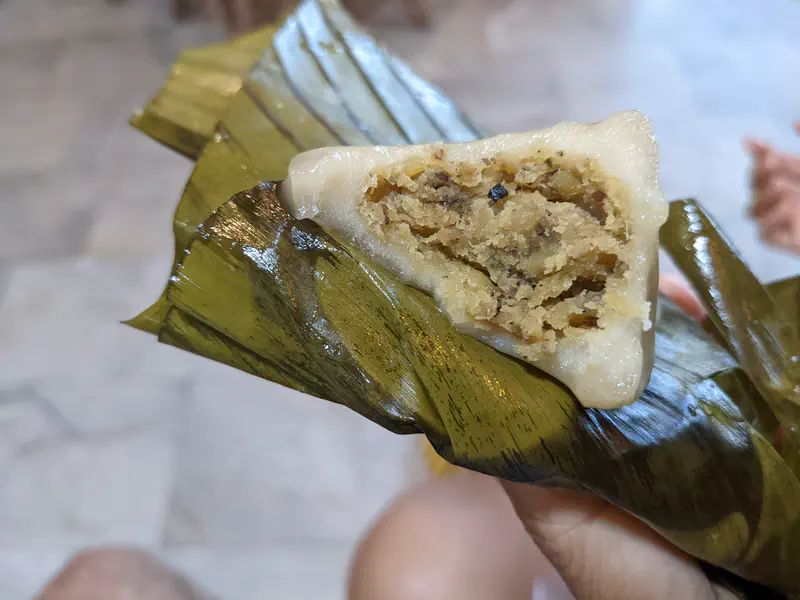 Close-up of a Thai dessert wrapped in banana leaf, showing a glutinous rice shell filled with sweet mung bean paste.