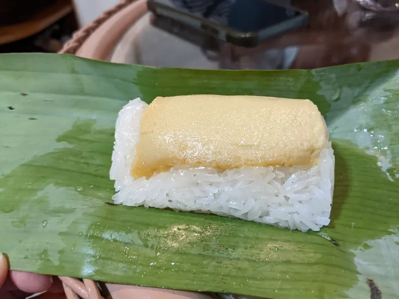 Thai dessert of white sticky rice topped with golden egg custard, served on a banana leaf.