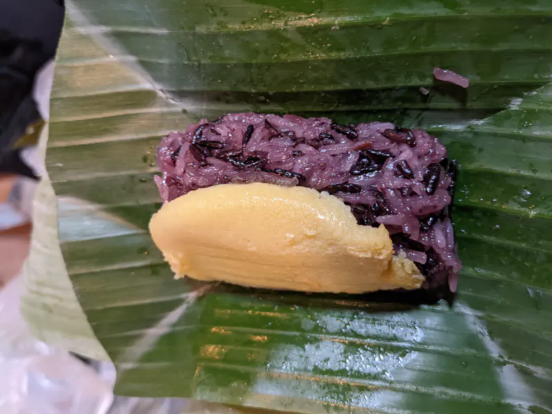 Traditional Thai dessert of black sticky rice topped with golden egg custard, served on a banana leaf.