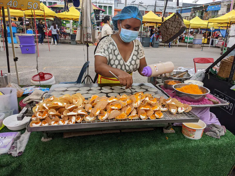 Street vendor preparing crispy Thai crepes with cream and golden egg yolk threads at a market stall.