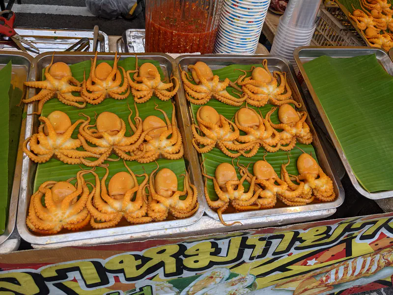 Trays of whole small orange octopuses neatly arranged on banana leaves at a street food stall.