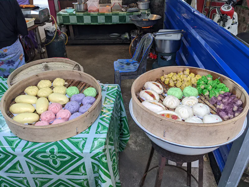 Large bamboo steamers filled with colorful buns and dumplings on display at a street market stall.