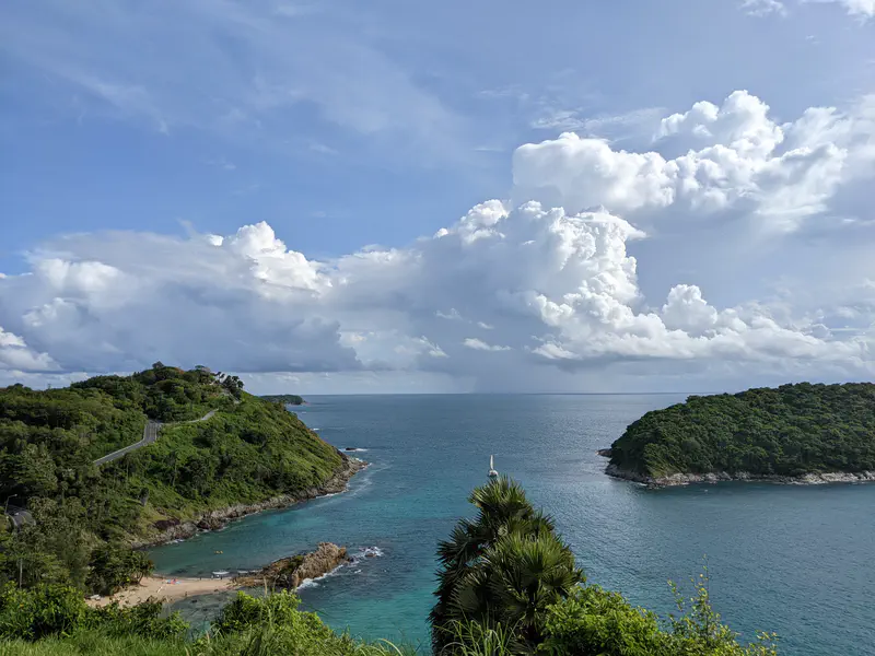 Coastal viewpoint overlooking green hills, small islands, and the blue ocean with dramatic clouds in the sky.
