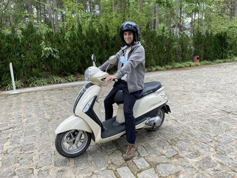 Person wearing a helmet sitting on a white scooter on a cobblestone path.