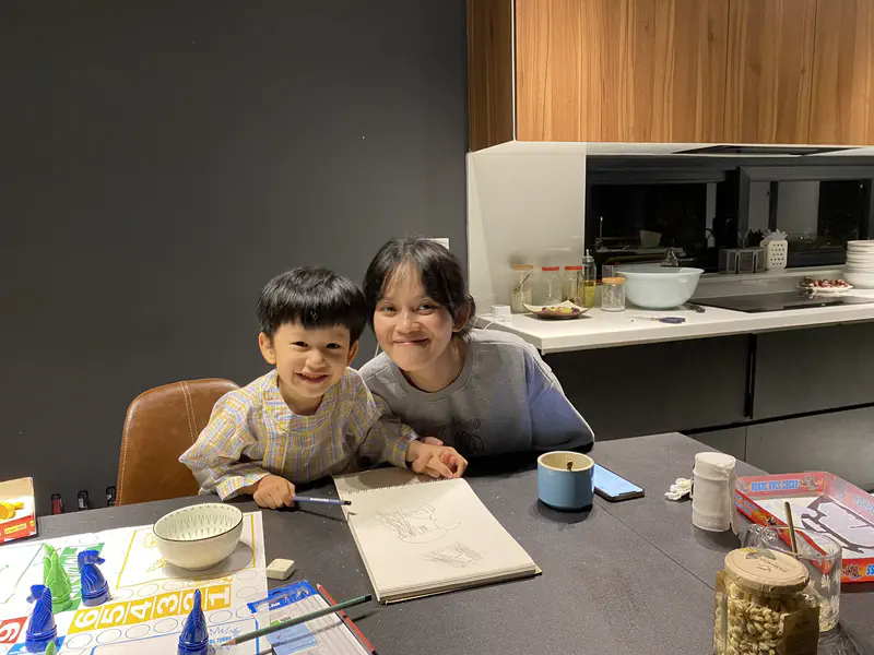 Smiling woman and child sitting at a table with drawings and board games.