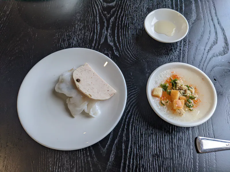 Vietnamese dishes on a black table, including steamed rice rolls with sausage and a small bowl of soup.