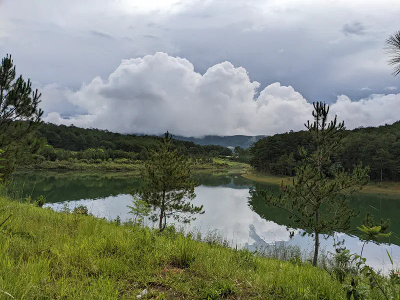 Lake reflecting dense clouds and surrounding green hills.