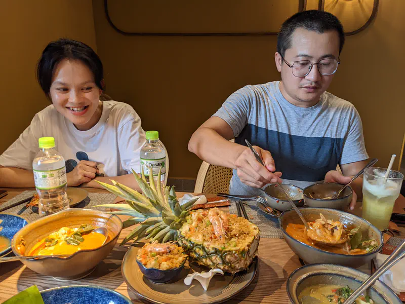 Two people at a restaurant table with dishes including pineapple fried rice and shrimp soup.