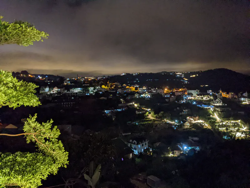 Nighttime cityscape of Đà Lạt with houses and streets lit up under cloudy skies.