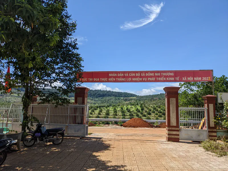 Entrance gate in Đồng Nai Thượng with a red banner and view of green hills in the background.