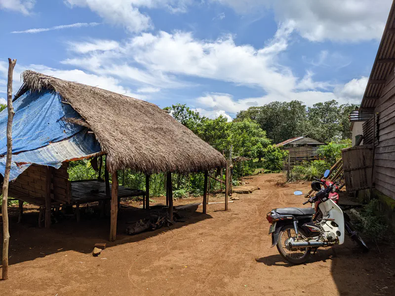 Thatched-roof shelter with a motorbike parked nearby in a rural yard.