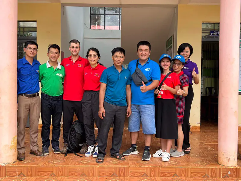 Group photo of people smiling and giving thumbs up in front of a building entrance.