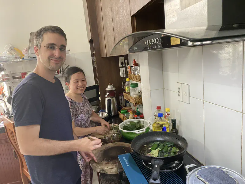 Two people cooking together in a kitchen, preparing food in a frying pan.