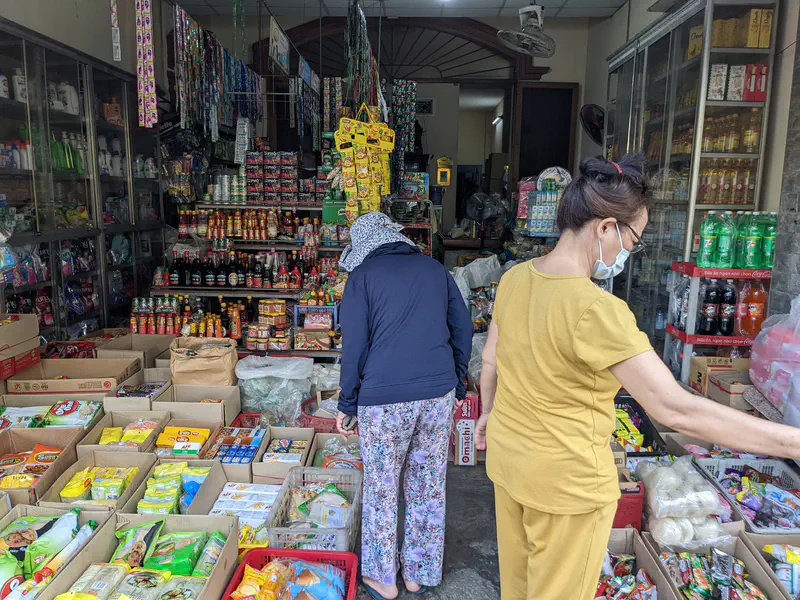 Small grocery store with shelves of packaged goods, condiments, and drinks, with two women shopping.