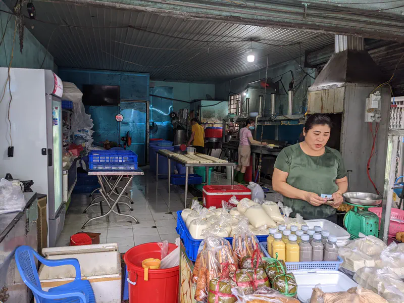 Shop with a woman selling tofu and soy products at the counter, with production area in the background.