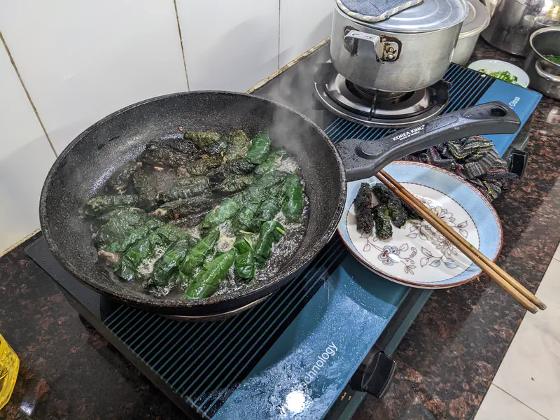 Close-up of green leaves being pan-fried on a stove in a black frying pan.
