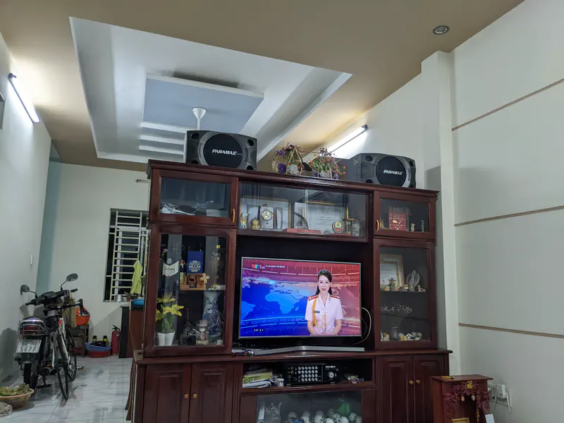 Television in a wooden cabinet showing a news anchor, with speakers and decorations on top.