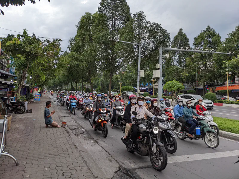 Crowd of motorbikes at a traffic light with a person kneeling and praying on the sidewalk.