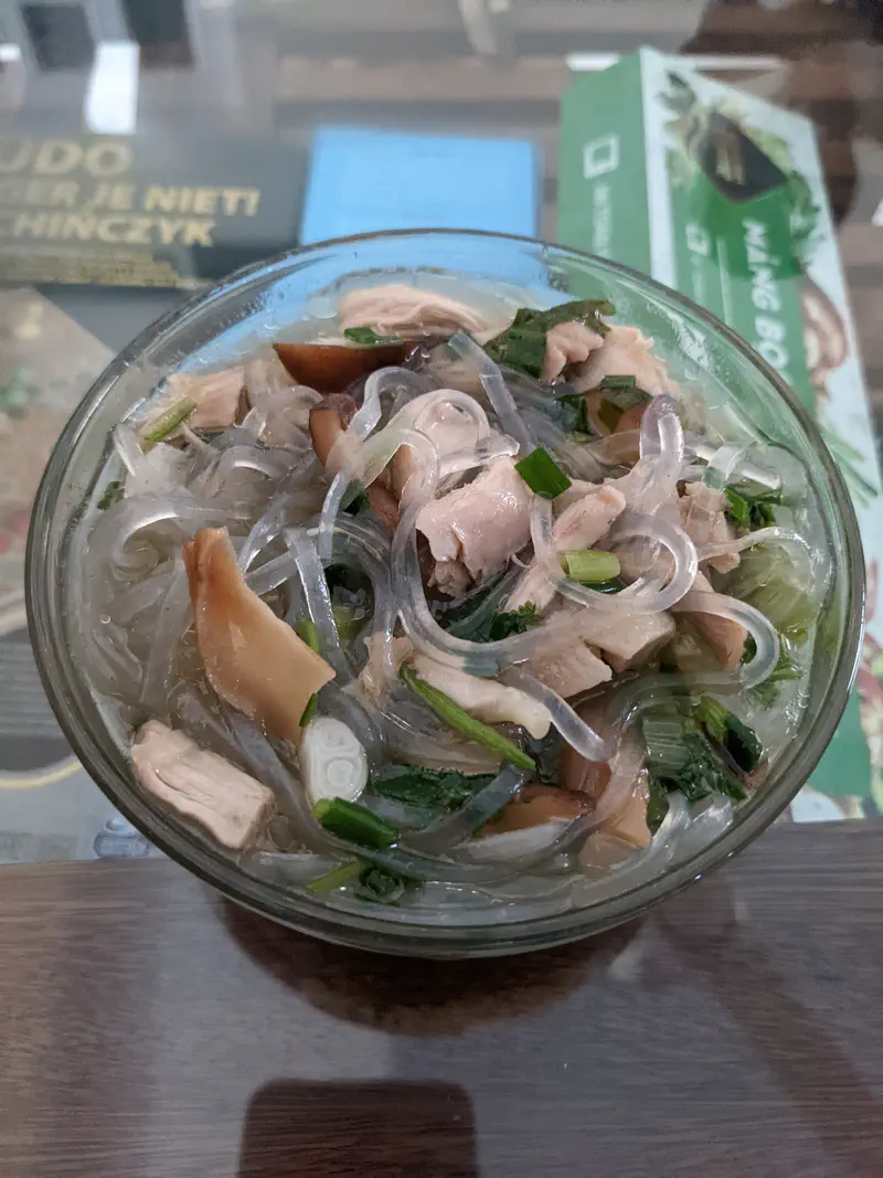Glass bowl of Vietnamese noodle soup with mushrooms, pork, herbs, and glass noodles.