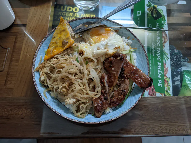 Plate of Vietnamese broken rice (cơm tấm) with grilled pork, shredded pork skin, steamed egg, and fried egg.