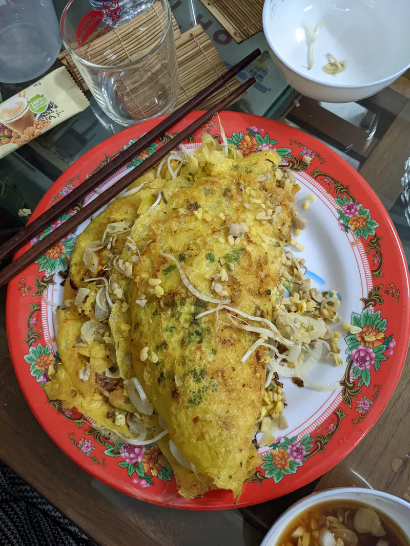 Vietnamese bánh xèo (crispy rice pancakes) filled with bean sprouts and meat on a colorful plate.