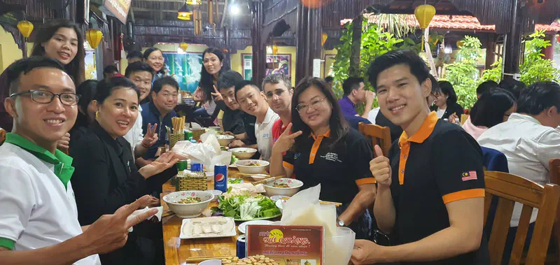 Group of people smiling and posing at a long table filled with Vietnamese dishes.