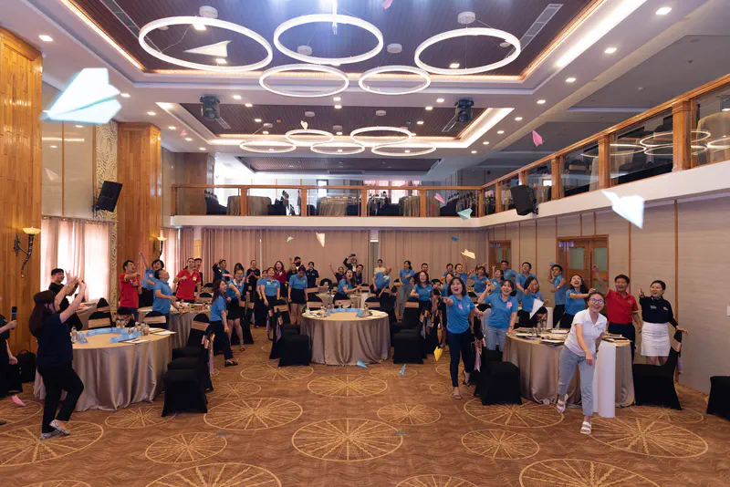 Group of people indoors throwing paper airplanes during a team activity.