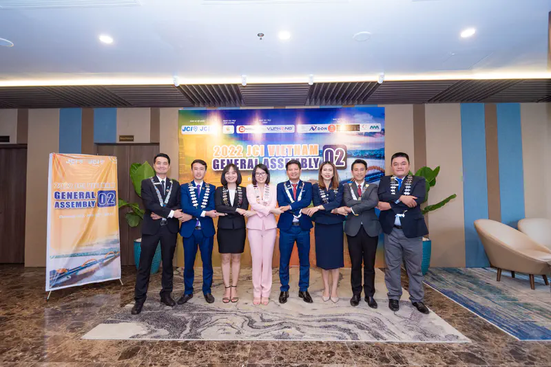 Group of JCI Vietnam members posing for a photo at the 2022 General Assembly in Da Nang City, standing arm-in-arm in front of the event banner.