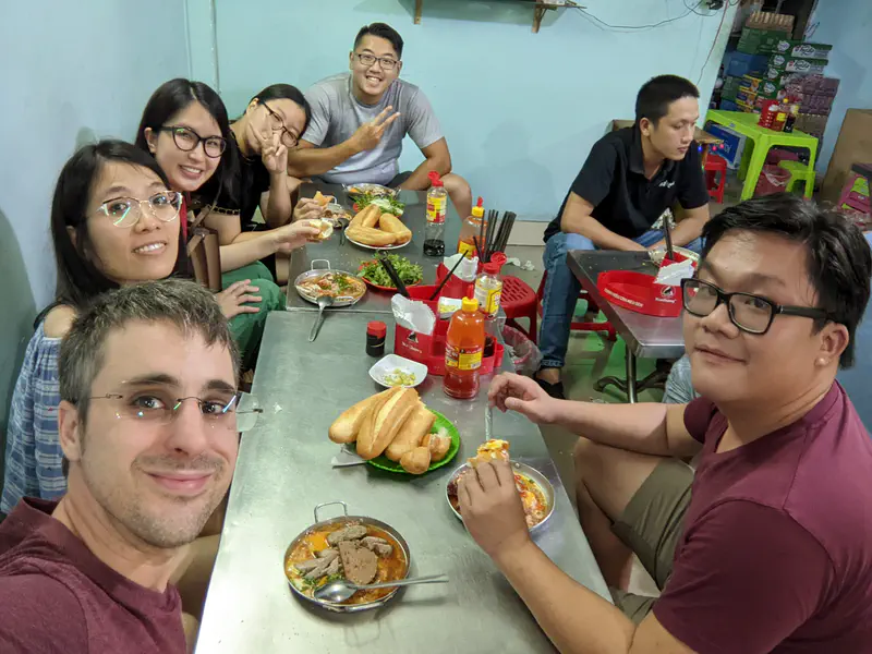 Friends at a small restaurant table enjoying bánh mì and other Vietnamese dishes.