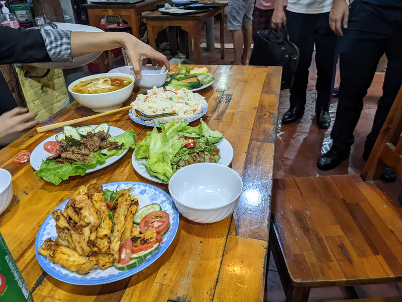 Plates of grilled meat, vegetables, rice, and soup on a wooden restaurant table.