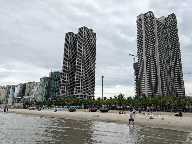 Beach scene with people near the shore and tall high-rise buildings in the background.
