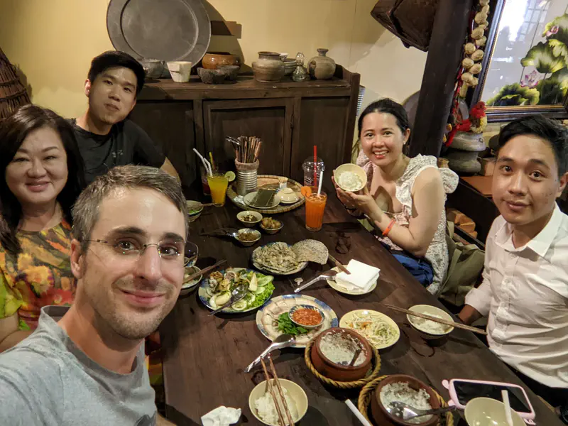 Group of five people smiling at a restaurant table with various Vietnamese dishes.