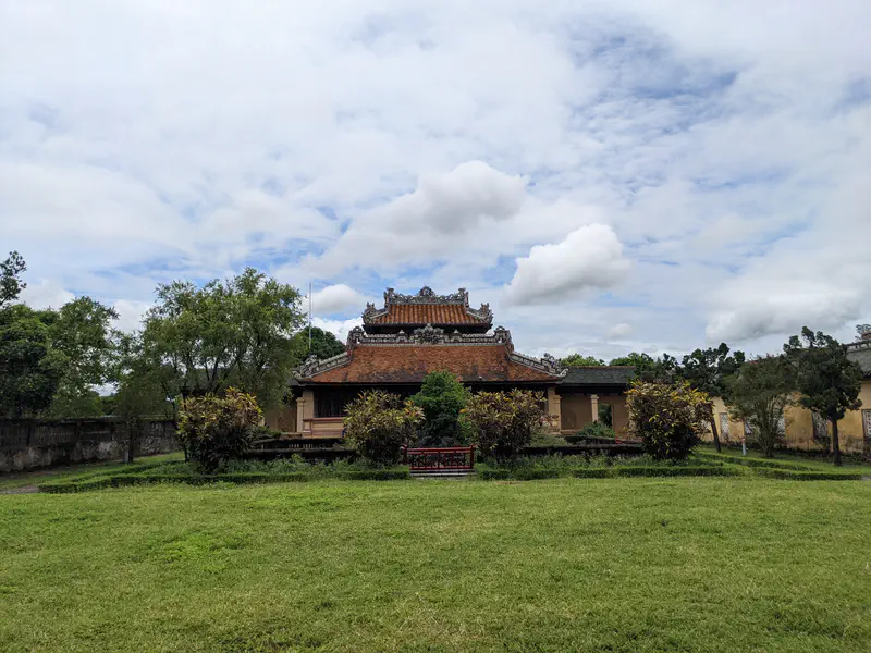Stone walkway leading through a red-walled gate toward another historic building in Hue.