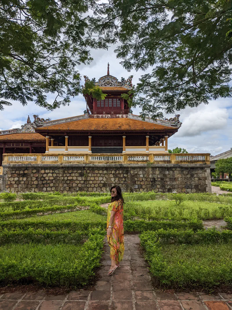 Woman in colorful dress standing in a garden path with an ancient palace in the background.