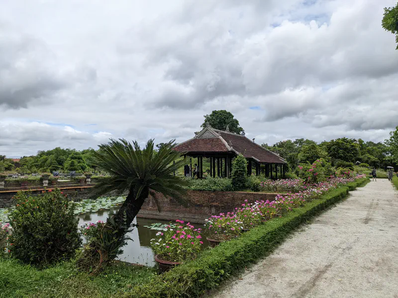 Traditional pavilion by a pond with blooming flowers in a historic garden.