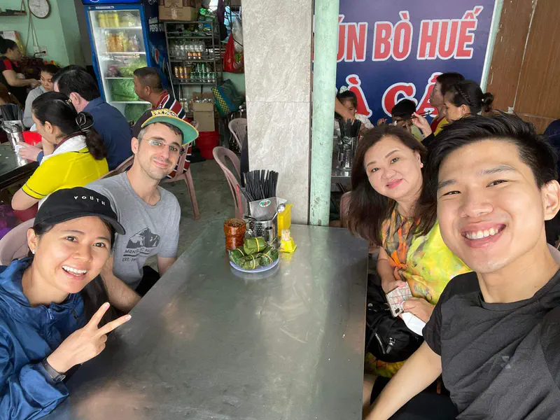 Group of four smiling people sitting at a table inside a busy Vietnamese restaurant.