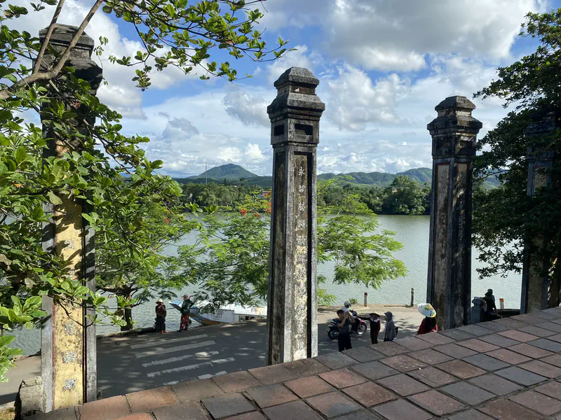 Scenic view from Thien Mu Pagoda overlooking the Perfume River, with ancient stone pillars and mountains in the background.