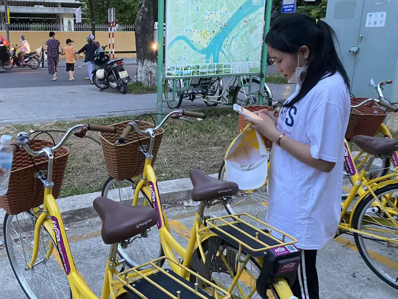 Young woman checking her phone next to parked yellow rental bicycles in Huế.