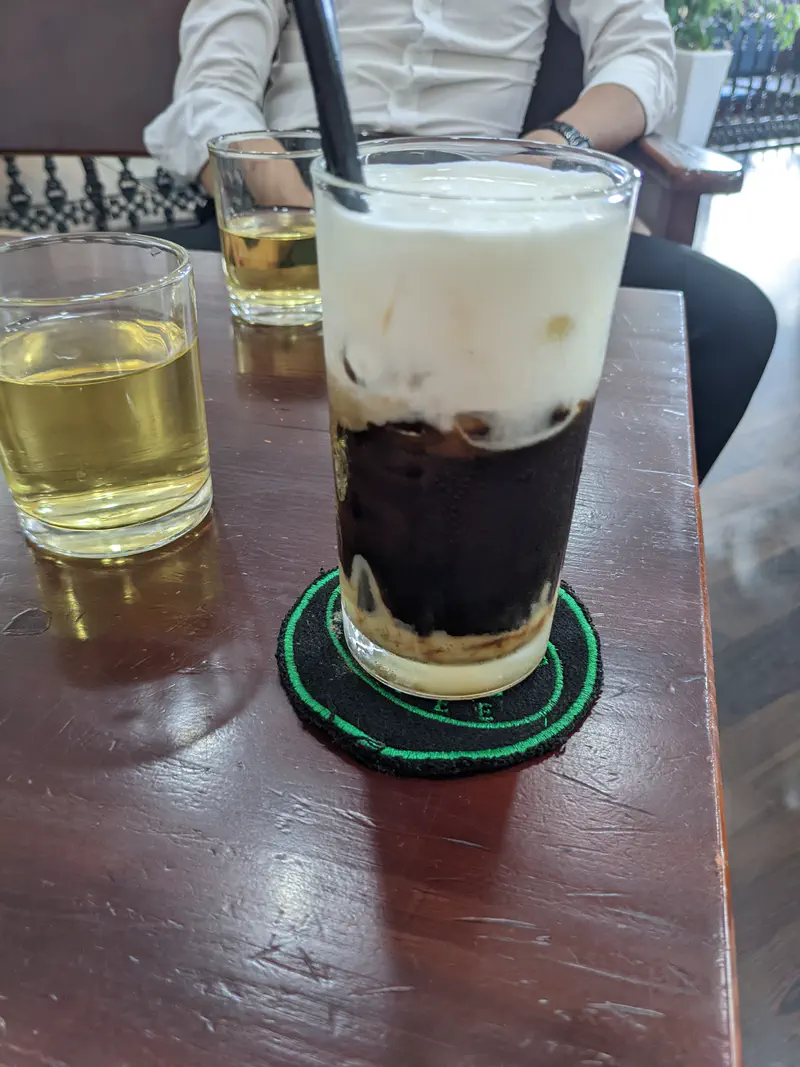 Glass of iced salted coffee with cream foam and two glasses of tea on a wooden table.