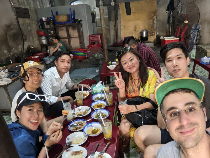 Group of six people smiling and posing around a table with dishes in a casual eatery.