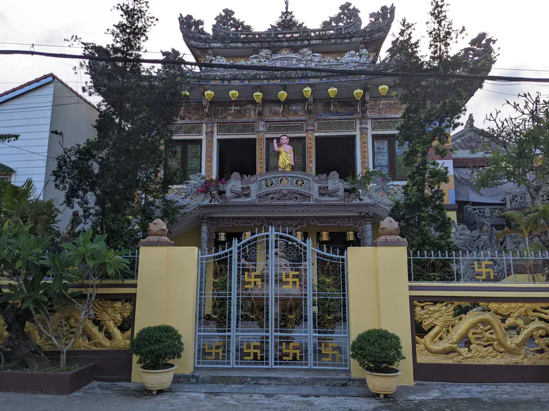 Ornate Buddhist temple with dragon carvings, yellow lanterns, and a statue of Buddha above the entrance.