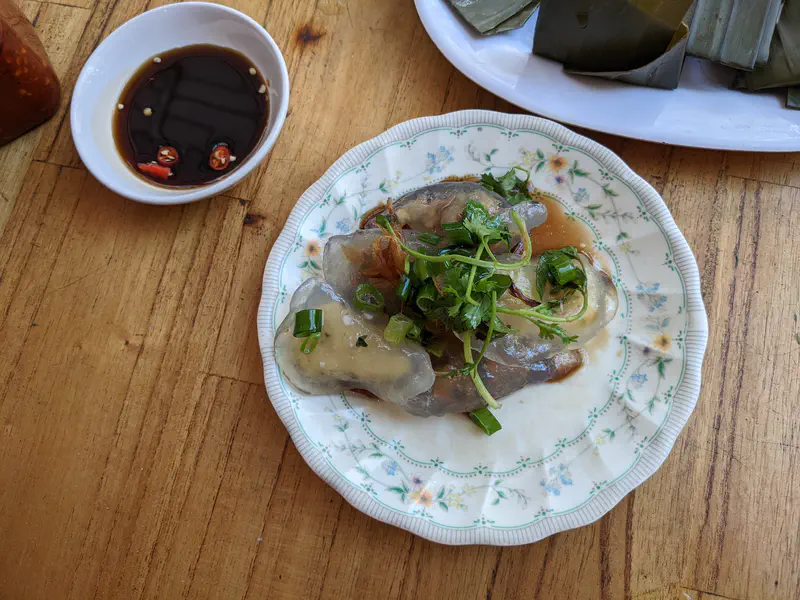 Plate of translucent Vietnamese dumplings topped with scallions and herbs, served with soy sauce and chili on the side.
