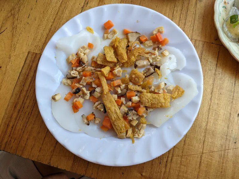 Plate of steamed rice cakes topped with diced carrots, mushrooms, tofu, and crispy fried pieces.