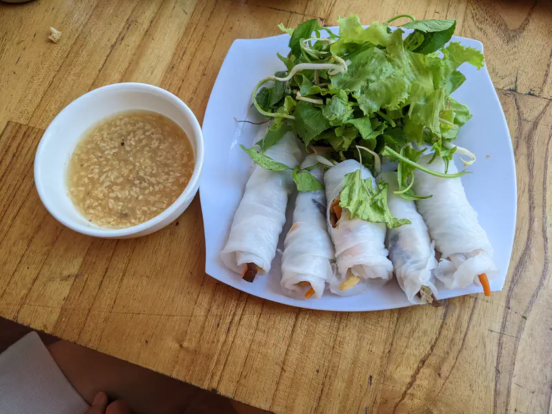 Plate of fresh spring rolls with lettuce and herbs, served with a bowl of sesame dipping sauce.