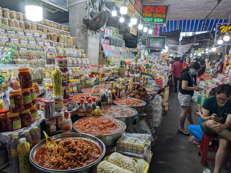 Bustling market stall with jars, bottles, and large bowls of pickled and spiced foods in Vietnam.