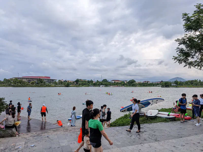 Crowd by the riverbank with people kayaking and paddleboarding on the water.