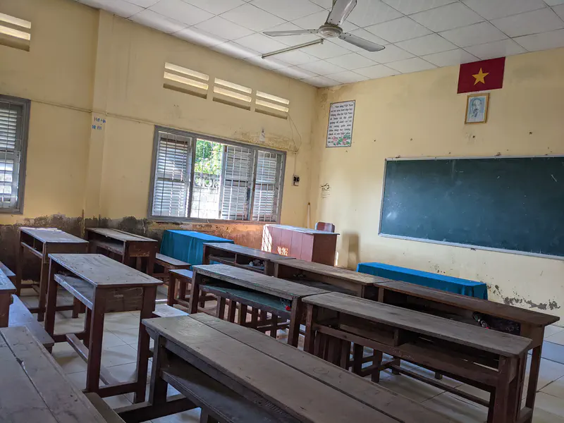 Empty classroom with wooden desks, chalkboard, and a Vietnamese flag on the wall.