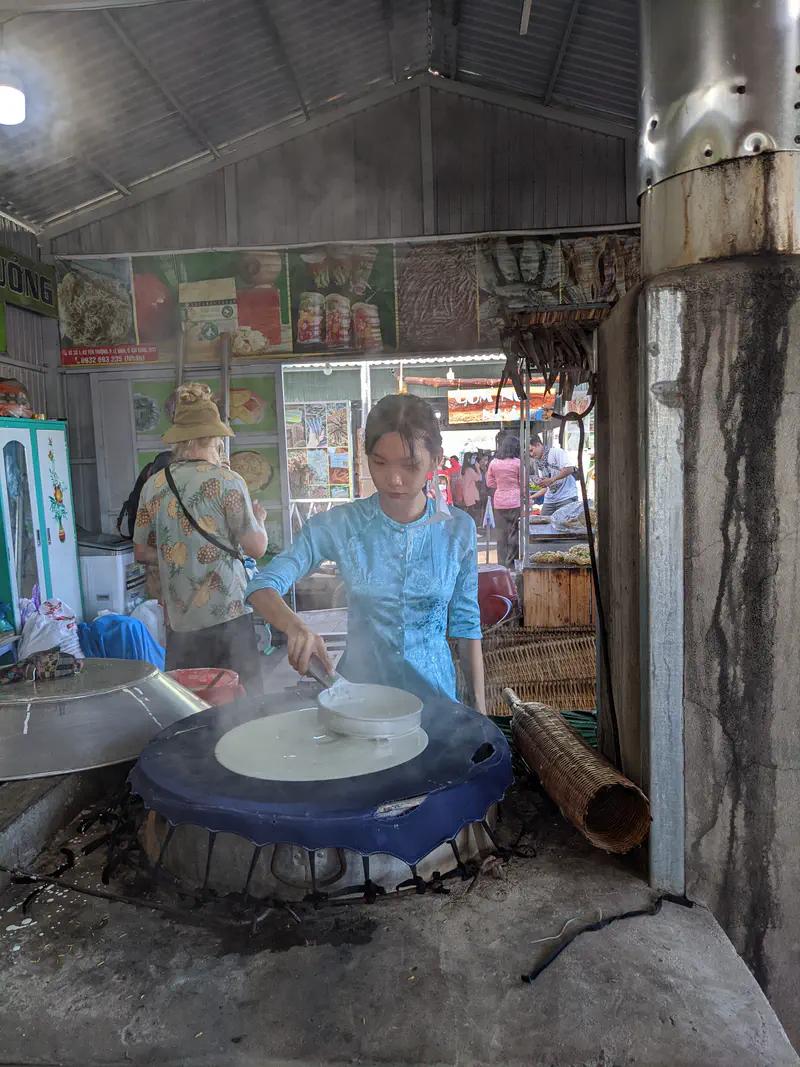 Vendor stir-frying noodles at a food stall while tourists watch.