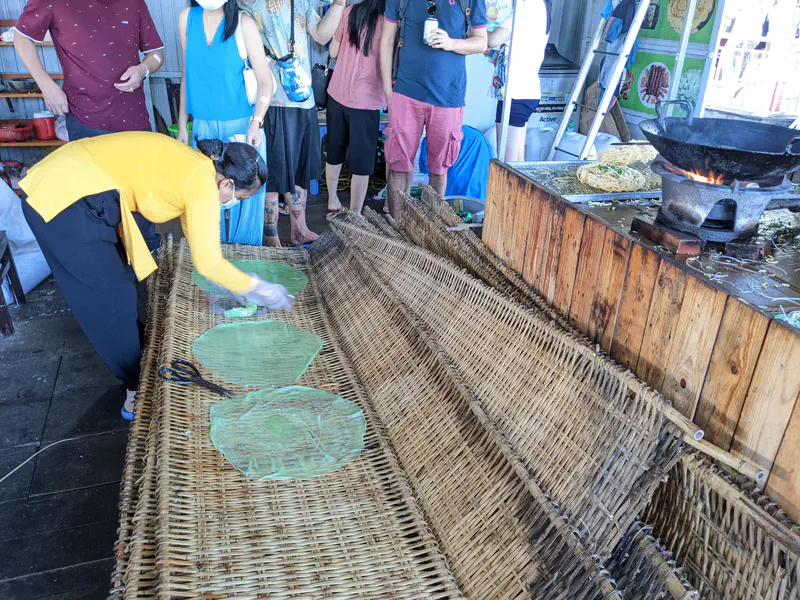 Worker placing green rice paper sheets on bamboo mats to dry.